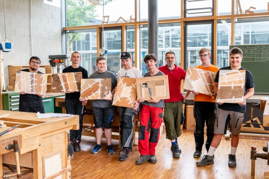 Lehrer und Schüler zeigen stolz ihre Holzobjekte.