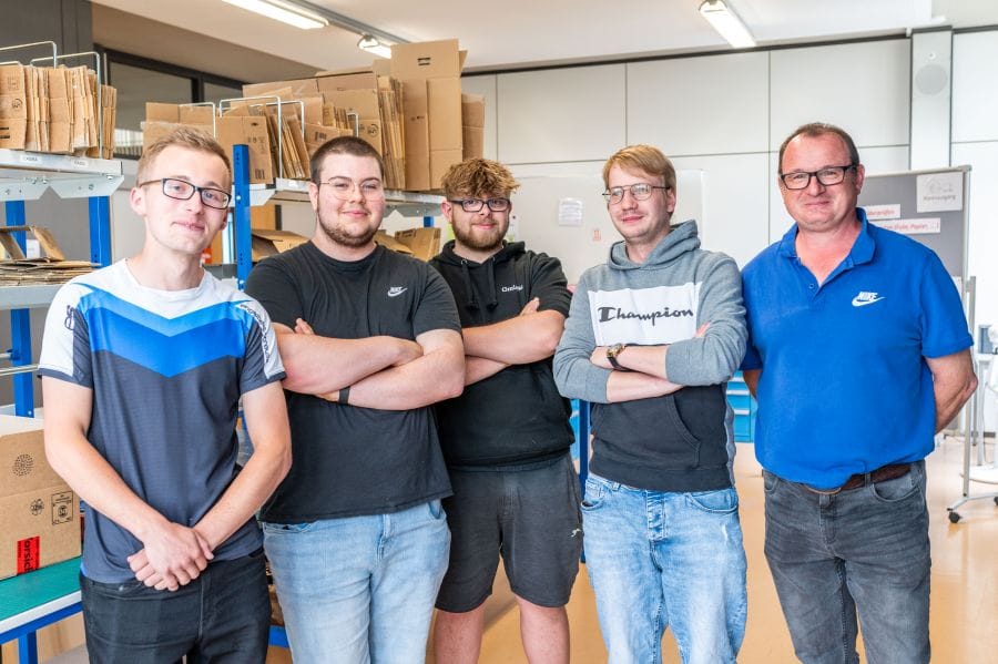 Lehrer und vier Schüler stehen in der Lagerhalle.