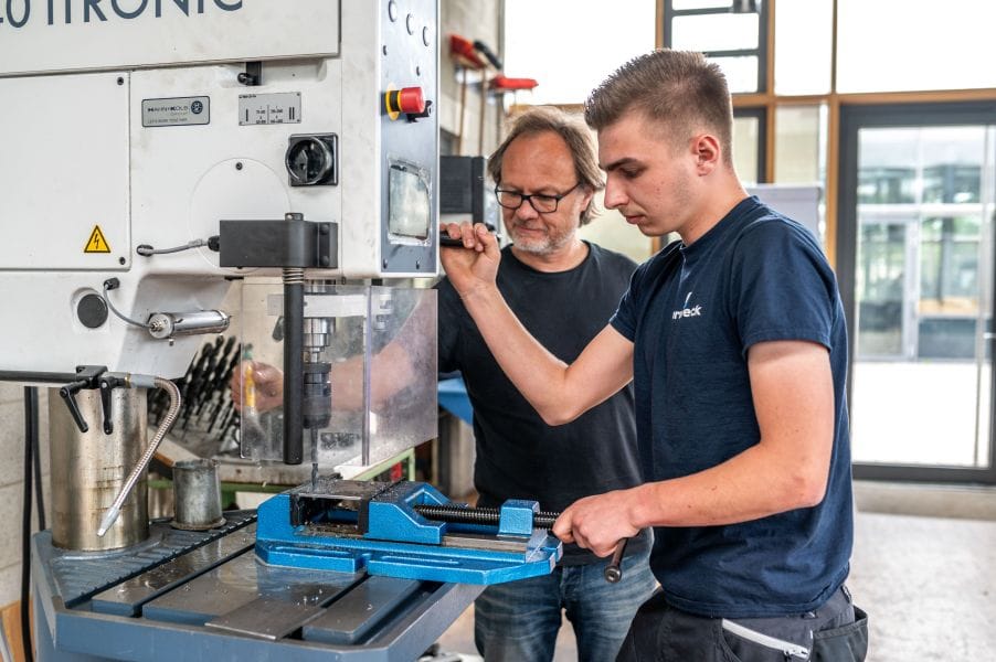 Lehrer und Schüler an einem Stanzgerät in der Fertigungshalle.
