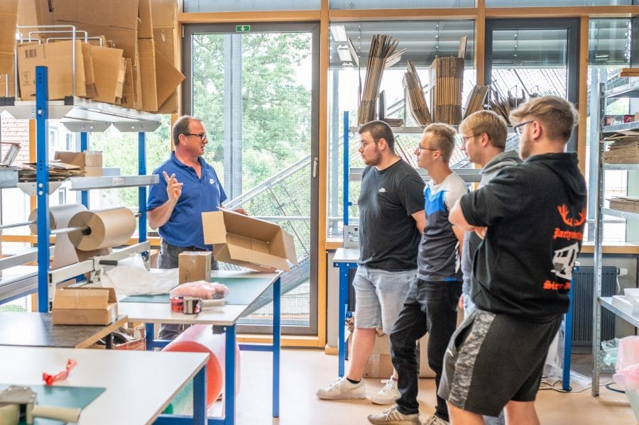 Lehrer erklärt die Lagerlogistik. 4 Schüler hören zu.