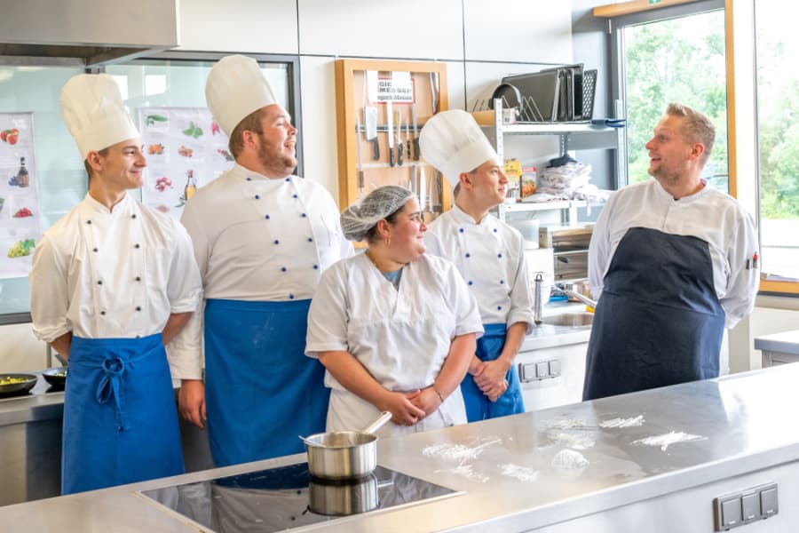 FünfKöche stehen in der Großküche und lachen